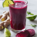beet lime ginger cleanse juice in a glass with beet slices, lime wedges, and fresh ginger