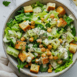 Vegan Caesar salad with romaine lettuce, creamy dairy-free Caesar dressing, roasted chickpeas, vegan parmesan, and golden croutons in a white bowl.