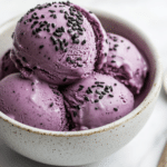 Creamy black sesame ice cream scoops topped with toasted black sesame seeds in a ceramic bowl.