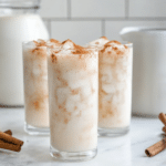 Creamy homemade horchata served over ice with cinnamon sticks and a dusting of ground cinnamon.